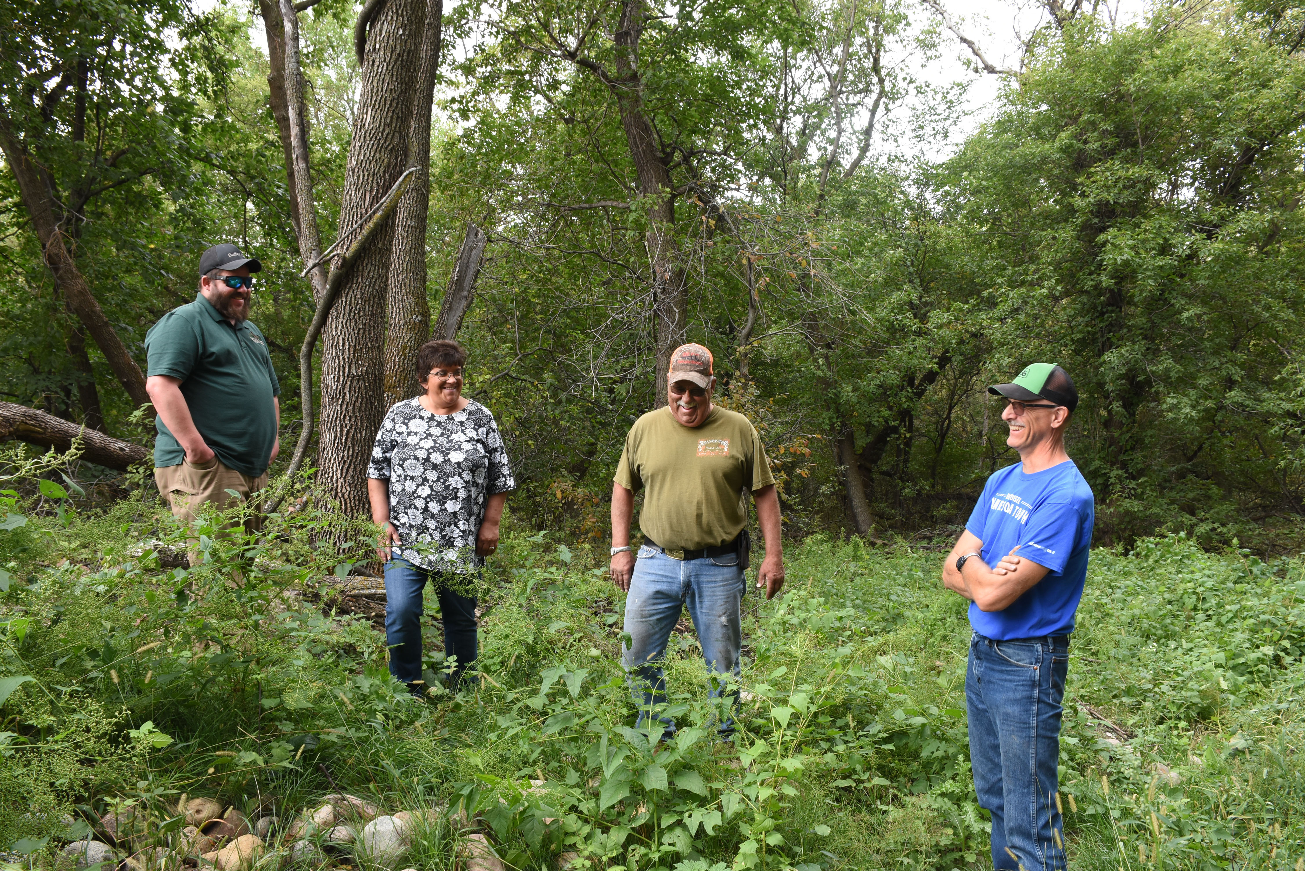 Four people stand in green plants with trees in the background