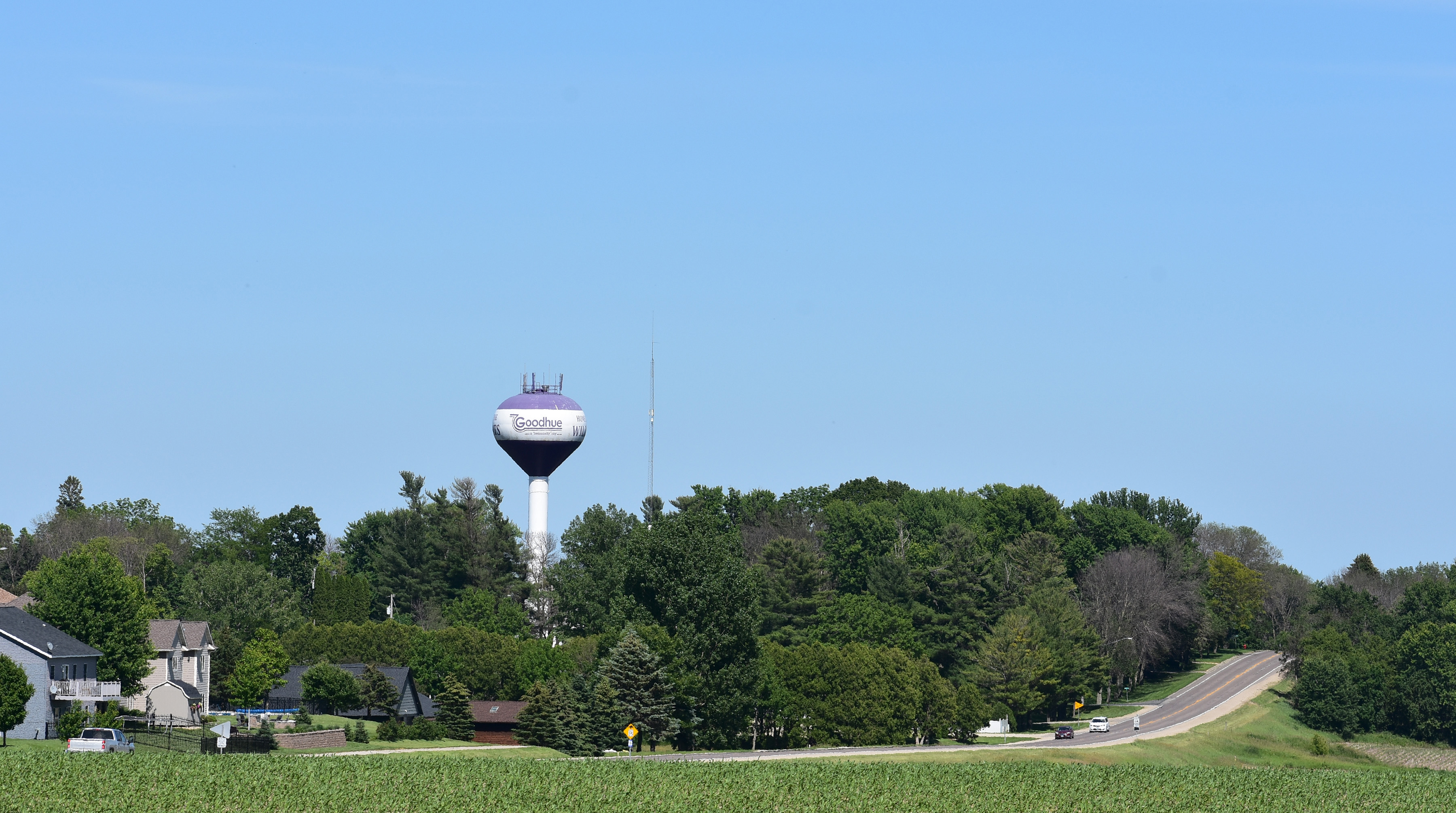 water tower behind trees, a highway and a corn field