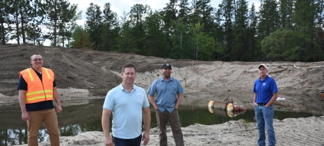 Four men stand in front of a pond filled with water