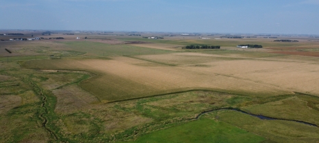 An aerial view of a farm field shows green and brown vegetation, plus a blue stream.