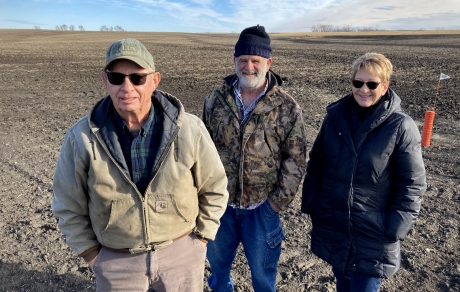 Three people stand in a field where black dirt shows construction has recently taken place
