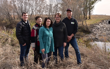 Five people stand in a group with a creek and a large square culvert in the background